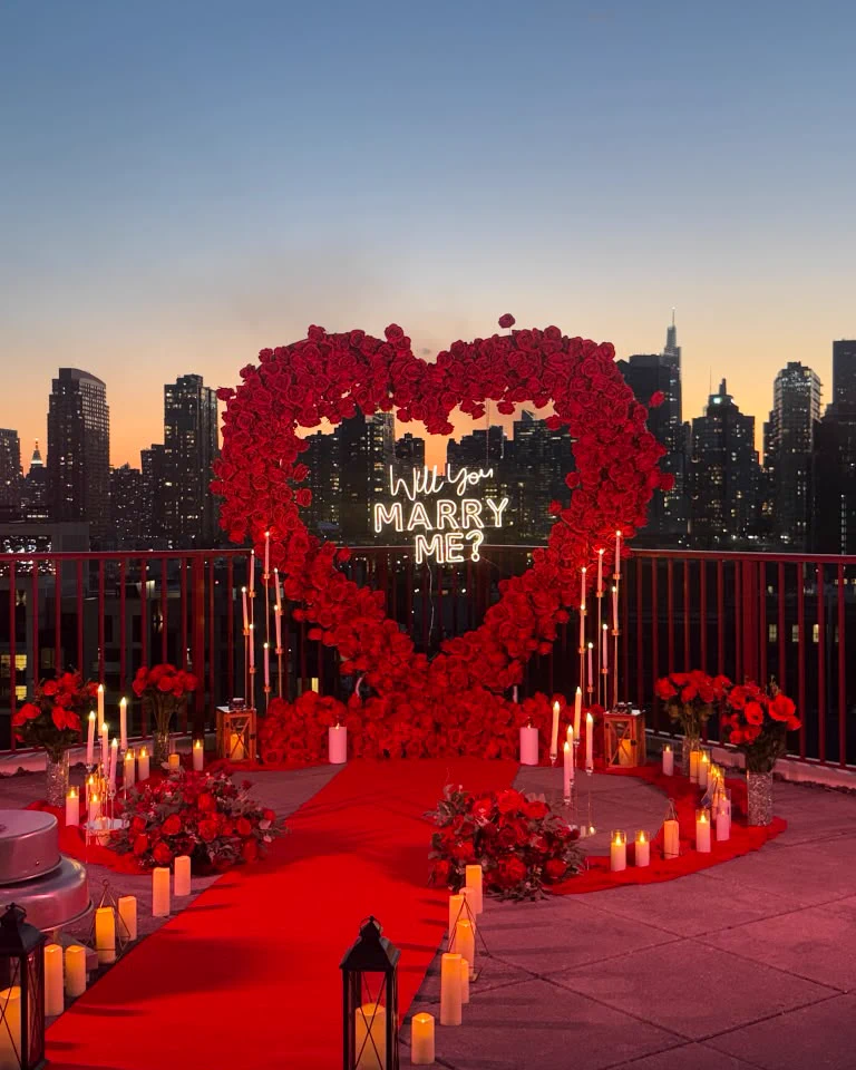 Corazón de rosas rojas y velas en un rooftop, con el skyline al anochecer